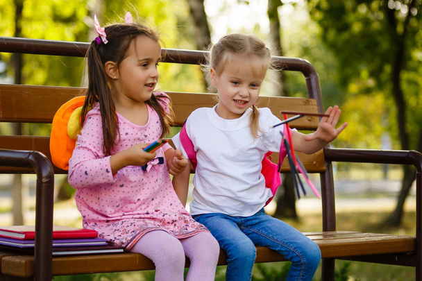 Adorable little school girls with pencils sitting on bench outdoor. - Fotó, kép
