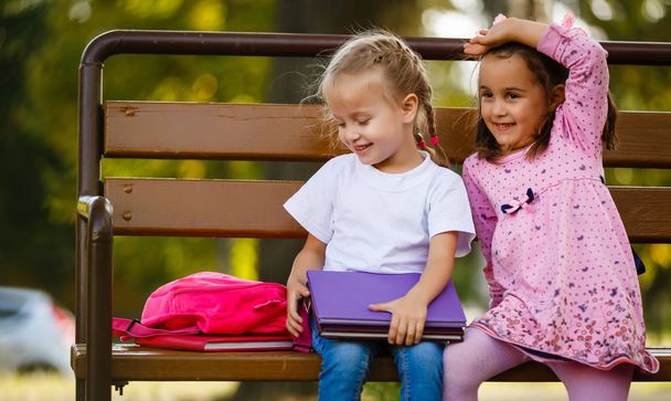 Две девушки с книгами сидят на скамейке в парке
 - Фото, изображение