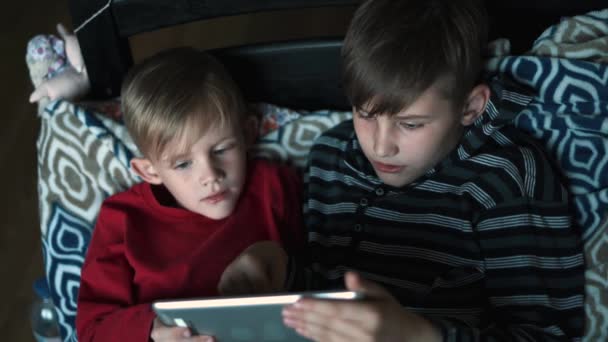 Dwoje dzieci za pomocą tabletu pc w domu w nocy. Bracia z komputera typu tablet w ciemnym pokoju. Dzieci, chłopcy gry na komputerze typu tablet, emocje. Przed snem. Gry komputerowe - Materiał filmowy, wideo