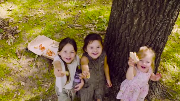 Três meninas de pé perto da árvore no parque e comer pizza
 - Filmagem, Vídeo