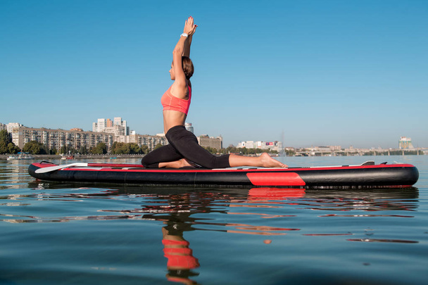  Woman practicing sitting variation of yoga pose on paddle board  - Fotografie, Obrázek