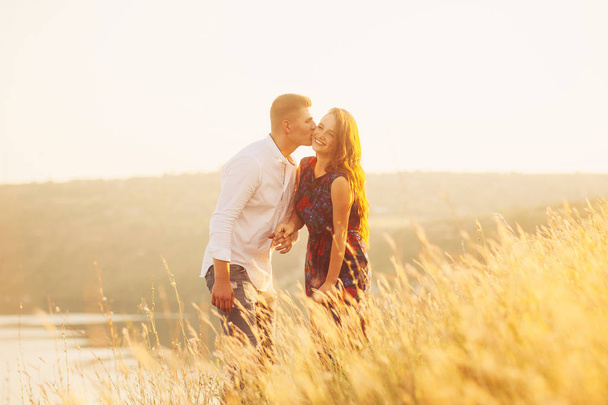 Молода пара насолоджується заходом сонця на лузі. В любові пара цілується і посміхається
 - Фото, зображення