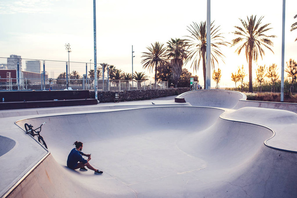 Photo of a young man using mobile phone while relaxing in the skate park. - Foto, Imagen