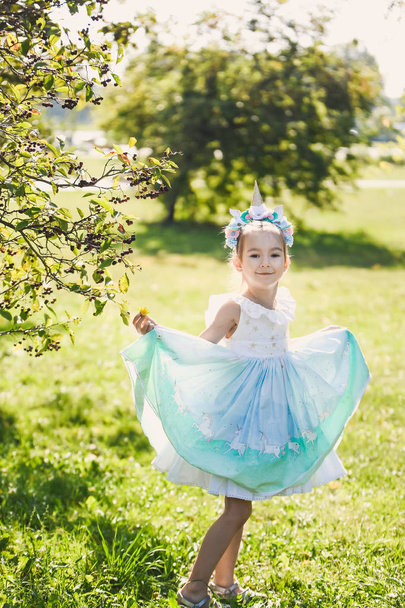 close-up portrait of a beautiful girl in a romantic blue cute dress with in a green autumn garden park  smiling sunny day celebrates Halloween with unicorn - Foto, Imagen