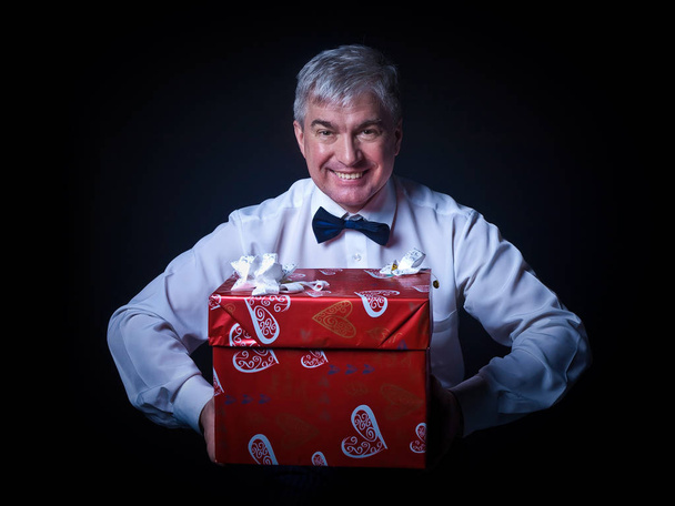A grey-hair red imposing respectable man with gifts. A handsome imposing respectable grey-hair ed man giving presents in red wrapping paperagainst a black background. - Fotoğraf, Görsel
