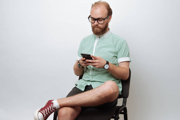 Bebaarde man aanbrengen op stoel en het gebruik van mobiele telefoon - Foto, afbeelding