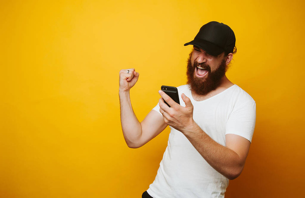 Счастливый бородач празднует успех и смотрит в телефон
 - Фото, изображение