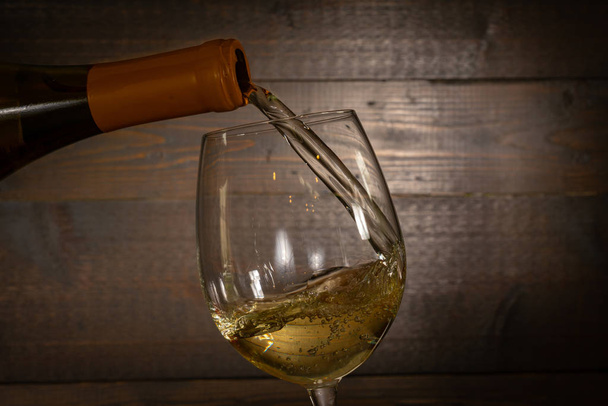 Witte wijn gieten in een wijnglas uit een fles - Foto, afbeelding
