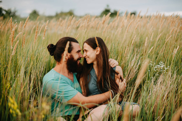 Happy couple looking at each other on a field outdoors smiling. In love bearded man with a long haired girl. - Photo, Image