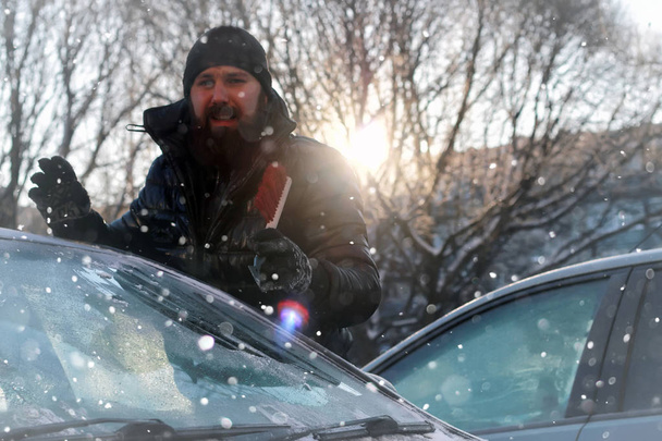 man cleans snow from the glass at the car - 写真・画像