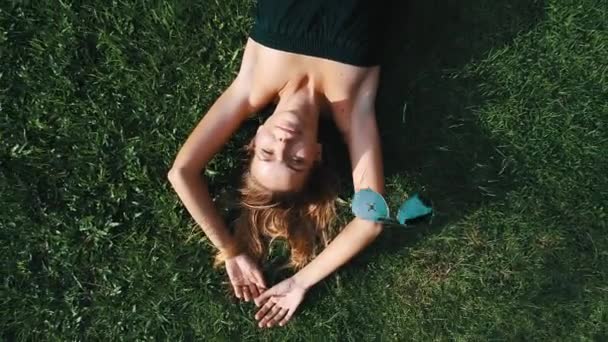 Вид сверху с воздуха на счастливую женщину, отдыхающую на траве в солнечный летний день. Дрон снимает солнцезащитные очки во время подготовки к летнему отдыху
 - Кадры, видео