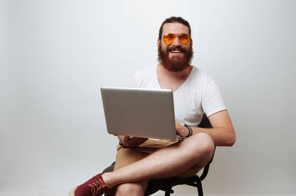 young bearded hipster man with beard sitting on chair and surfing internet on laptop pc. Handsome guy enjoying online communication using gadget - Photo, Image