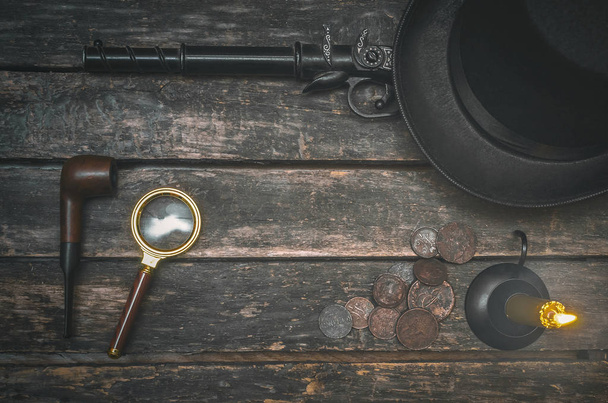 Musket gun, smoking pipe, magnifying glass, money, bowler hat and burning candle on wooden table background. Detective agent table. - Photo, Image
