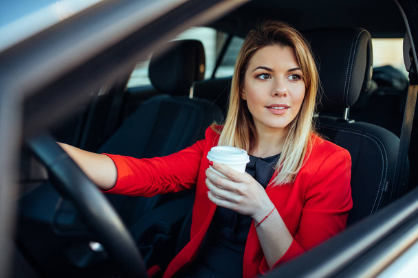 Foto einer lächelnden Geschäftsfrau im Auto, die Kaffee trinkt. - Foto, Bild