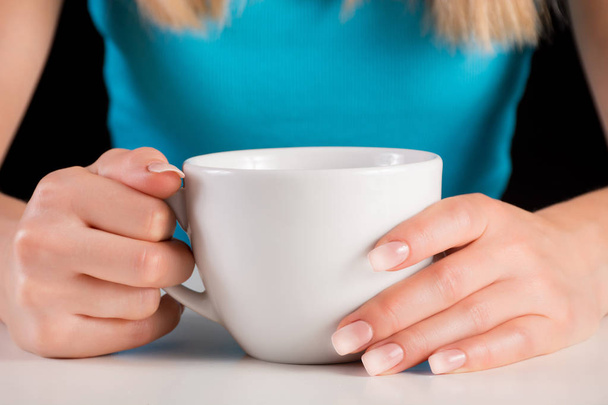 Frau Hände mit ombre Maniküre hält Tasse Kaffee oder Tee auf weißem Schreibtisch. Schönheits- und Manikürkonzeptbild. Nahaufnahme, selektiver Fokus - Foto, Bild