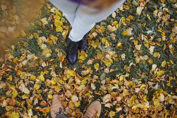 Boots of a man and a woman against a background yellow autumn leaves. Male and female legs. Top view. - Фото, зображення
