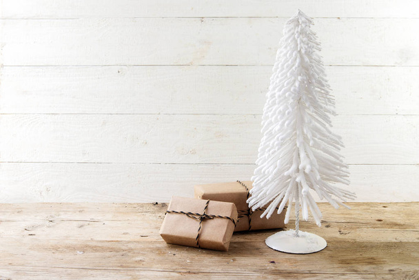 kleine kerstboom uit Wit gevlekt draad en giften in kraftpapier op een rustieke houten tafel, wit geschilderd vintage achtergrond met grote exemplaar ruimte, geselecteerd van focus - Foto, afbeelding