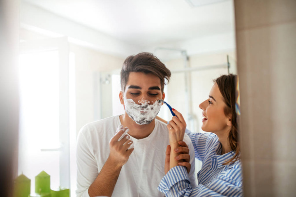 Portrait of a beautiful young couple having fun in the bathroom with shaving foam. - Zdjęcie, obraz