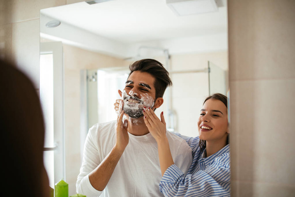 Portrait d'un jeune couple s'amusant avec de la mousse à raser dans la salle de bain
. - Photo, image