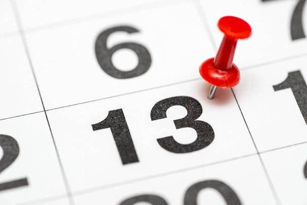 Pin auf der Datumsnummer 13. Der dreizehnte Tag des Monats ist mit einer roten Daumennadel markiert. Anstecknadel im Kalender - Foto, Bild