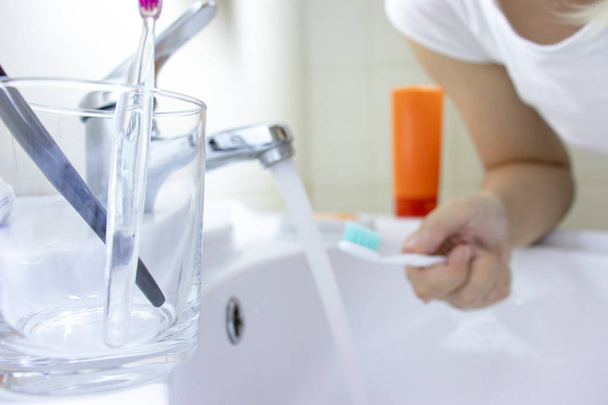 Clear glass with two toothbrushes in it, blurred woman with a toothbrush on background. - Foto, afbeelding