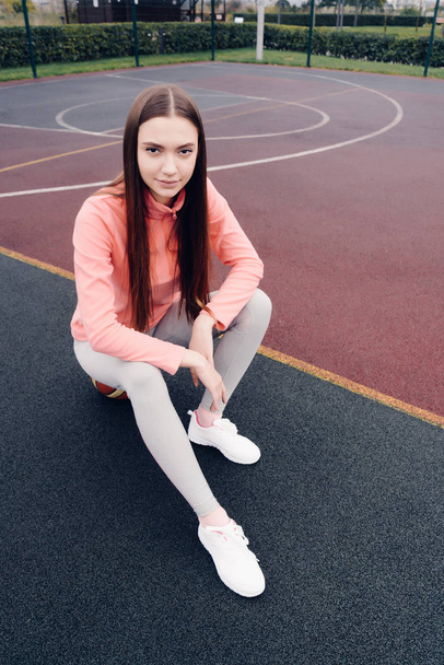 confident long-haired girl in a pink jacket resting on an outdoor sports field - Foto, Imagem