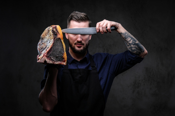 Cuoco cuoco tiene il coltello e grande pezzo di salumi esclusivi su uno sfondo scuro
. - Foto, immagini