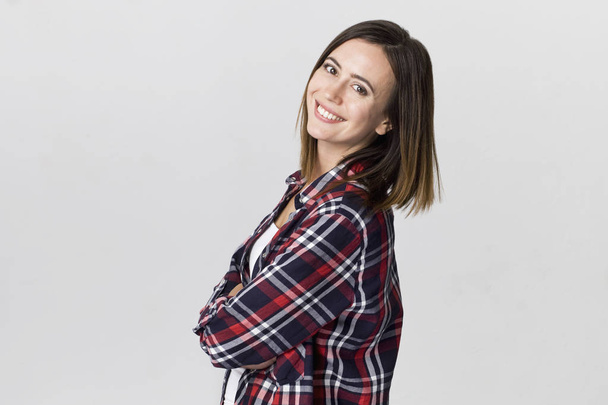 Smiling positive female with attractive look, wearing checkered shirt, posing against white blank wall - Photo, Image