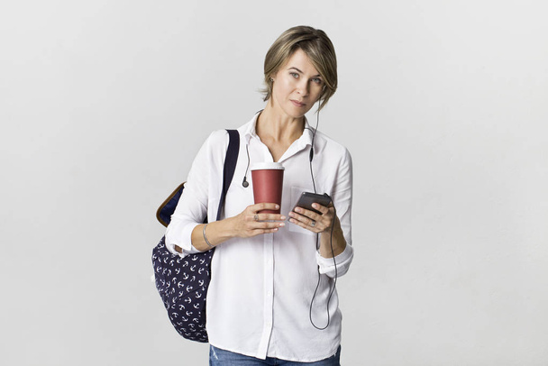Young women in white shirt, holding smartphone and cup of coffee, isolated - Фото, изображение