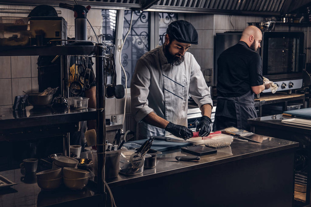 Two brutal cooks dressed in uniforms preparing sushi in a kitchen. - Fotoğraf, Görsel