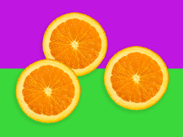 Slices of orange fruit isolated on colorful purple and green pastel background - fresh modern minimalistic and creative image - Photo, image