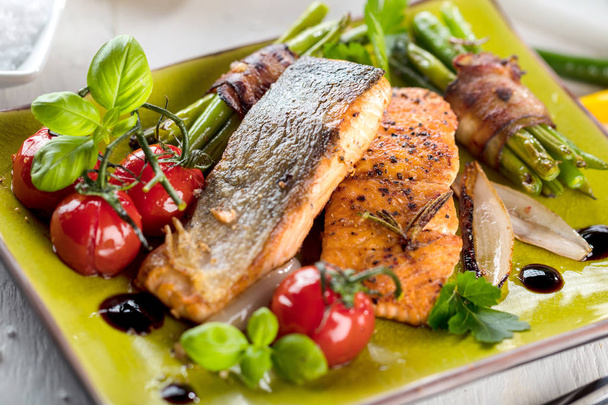 Гриль лосось с овощами подается на зеленой каменной тарелке на деревянном столе
  - Фото, изображение