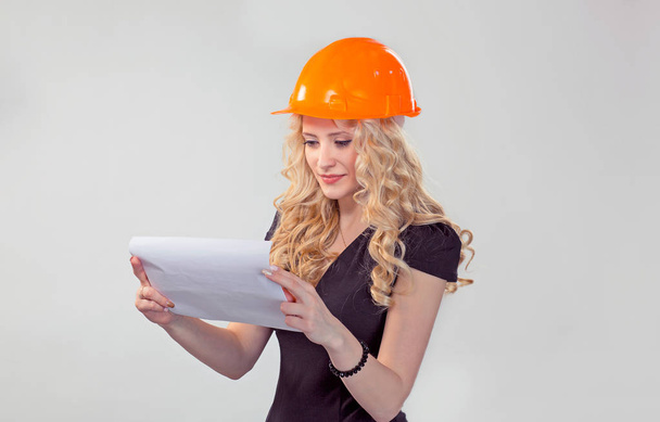Architect lady. Portrait of attractive woman in helmet cap, looking at architectural plan of building construction, isolated in white gray background. Positive face expression. Working hours lifestyle - Foto, Imagem