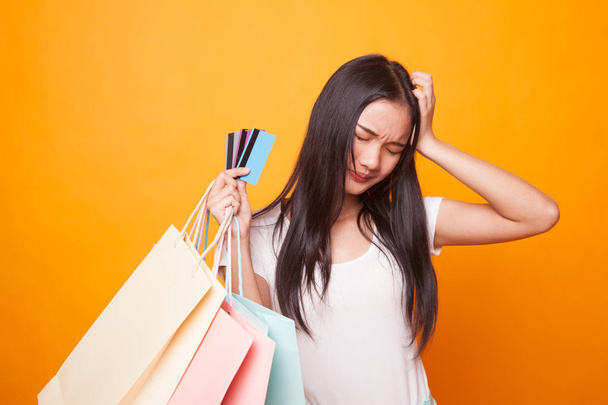 Unhappy  young Asian woman with shopping bags and credit card on bright yellow background - Fotografie, Obrázek