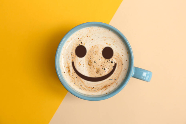 Cup of delicious hot coffee with foam and smile on color background, top view. Happy morning, good mood, inspiration - Photo, Image