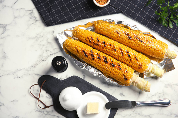 Fresh grilled tasty corn cobs served with butter on marble table, top view - Foto, Imagem