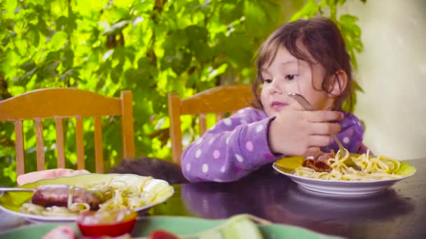 zwei freche Mädchen sitzen am Tisch und essen Pasta und Bratwurst - Filmmaterial, Video