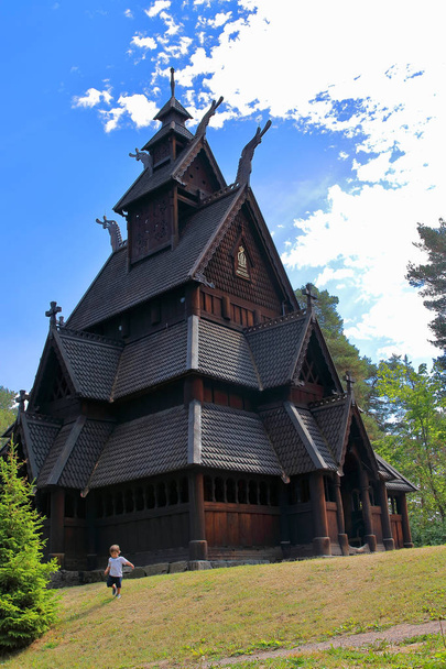Trochę dwa lata chłopiec działa i gra przed kościołem Gol, drewniany kościół pierwotnie zbudowany w mieście Gol, ale teraz znajduje się w norweskim Muzeum historii kultury o Bygdoy w Oslo, Norwegia - Zdjęcie, obraz