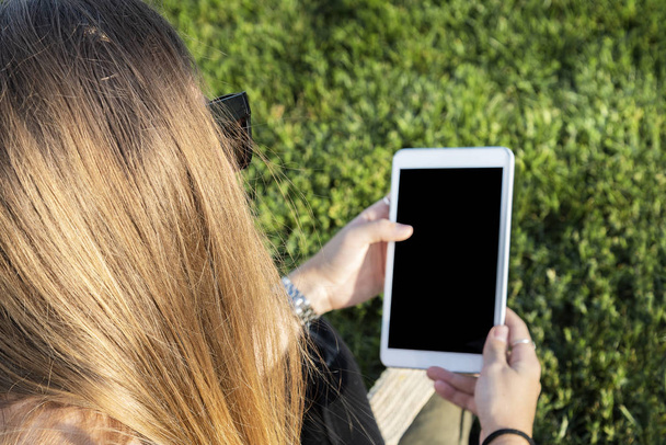 Όμορφη νεαρή κοπέλα, χρησιμοποιώντας ένα tablet στο ηλιοβασίλεμα, στο πάρκο. Χαλαρωτικό έννοια. - Φωτογραφία, εικόνα