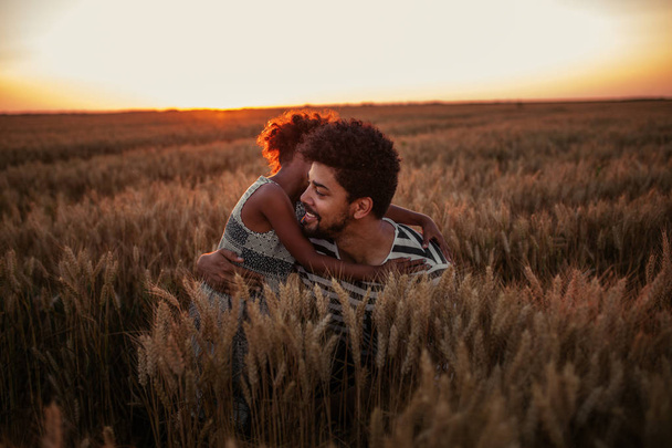 Portrait of an african american father and daughter hugging in the wheat field at sunset. - Fotoğraf, Görsel
