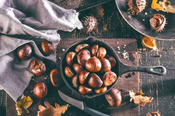 Roasted chestnuts in special perforated pan on old wooden table - Fotografie, Obrázek