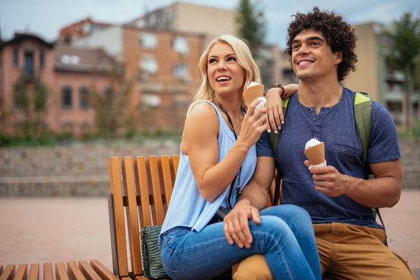 Young couple eating ice cream on a bench and enjoying in the town scenery. - Foto, Imagem