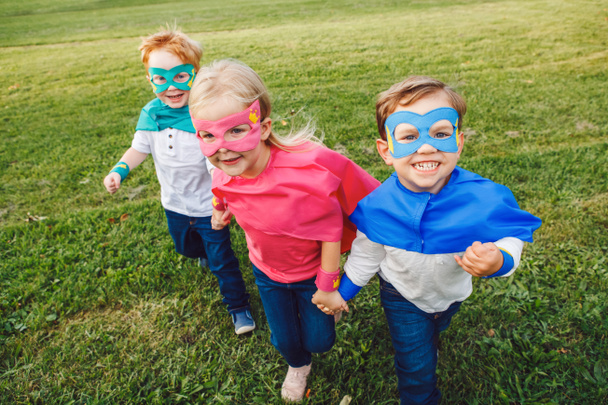 Cute adorable preschool Caucasian children playing superheroes. Three kids friends having fun together and running outdoors in park. Happy active childhood and friendship concept.  - Photo, Image