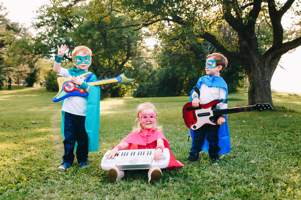 Sevimli sevimli okul öncesi beyaz çocuklar süper kahramanlar müzik oyun rock grubu Grup. Üç arkadaş eğlenceli park açık havada yiyorsunuz çocuklar. Mutlu etkin çocukluk ve dostluk kavramı. - Fotoğraf, Görsel