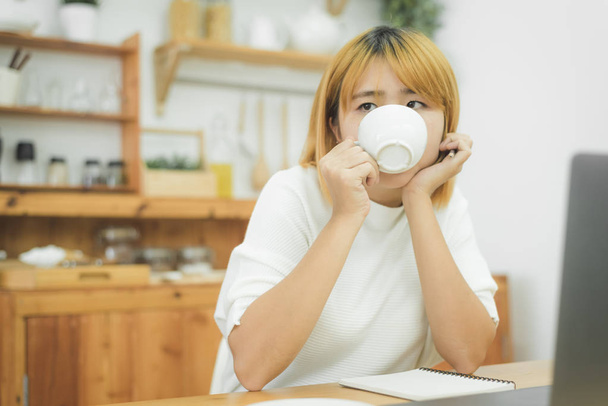 Piękna młoda kobieta uśmiechający się pracy na laptopie podziwiając picie ciepłej kawy siedząc w salonie w domu. Ciesząc się czas w domu. Azjatycki biznes kobieta pracuje w jej domu biura. - Zdjęcie, obraz