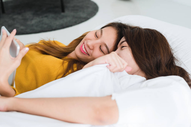 Jonge lesbische paar Aziatische vrouwen liggen op het bed naast elkaar samen met een emotie van liefde en gelukkig. LGBT paar geven haar vriendin een knuffel van liefde. LGBT transseksuele lover op het bed concept. - Foto, afbeelding