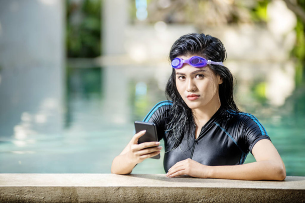 Young asian woman with swimsuit using mobile phone on the poolside - Фото, зображення