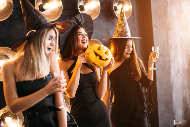 three cheerful young women in witch halloween costumes with pumpkin - Photo, image
