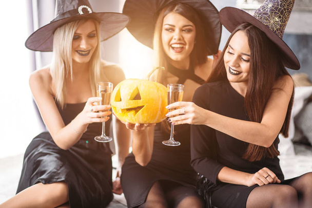three friends sit on bed and drink champagne Halloween party - Foto, Bild