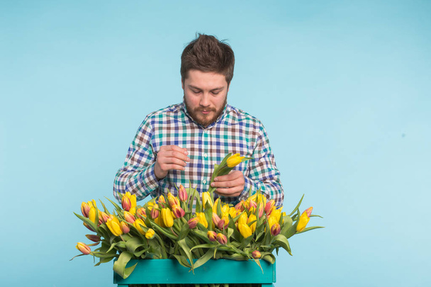 Handsome man fixing a bouquet of flowers on blue background - Foto, Imagem